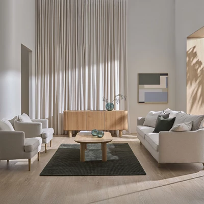 Ljust vardagsrum med soffa, fåtöljer, soffbord och sideboard.