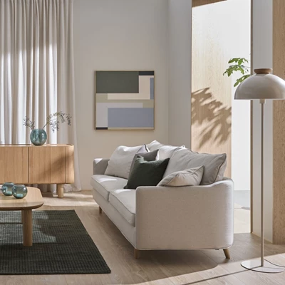 Inblick i ett ljust och nordiskt vardagsrum med soffa, golvlampa och sideboard.