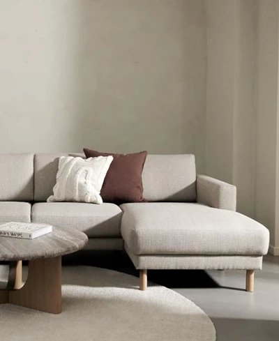 Beige chaiselongsoffa med soffbord och runt matta.