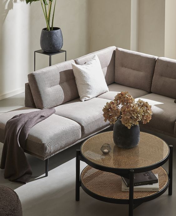 Hörnsoffa i grått med soffbord, piedestal med vas och annan inredning.