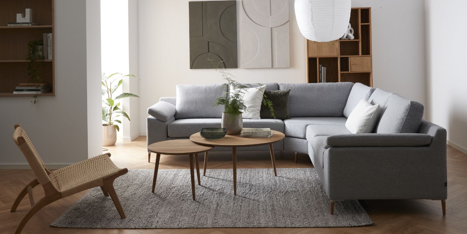 Vardagsrum med grå hörnsoffa, satsbord, fåtölj och diverse dekoration på väggen.