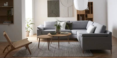 Flex.jpg (1) Vardagsrum med grå hörnsoffa, satsbord, fåtölj och diverse dekoration på väggen.