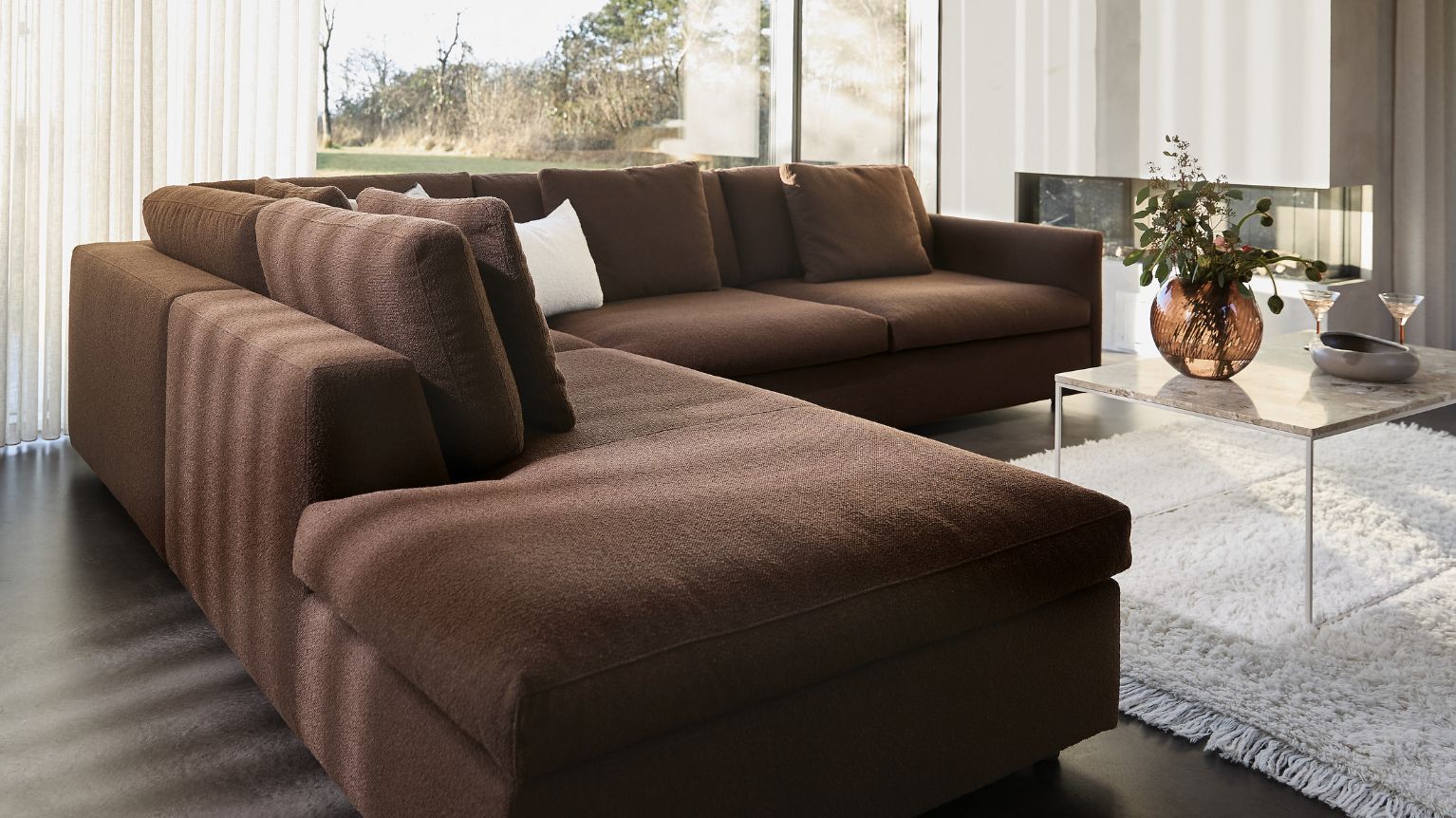 Brun chaiselongsoffa i vardagsrum med vitt golvmatta och soffbord.