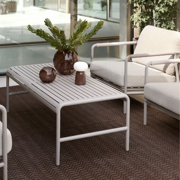 Närbild av ett loungebord i grått som står på en röd matta på terrassen