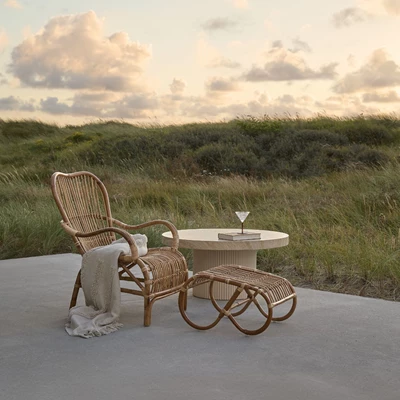 Fåtölj i naturlattan med pall stående på en terrass med natursanddyner i bakgrunden