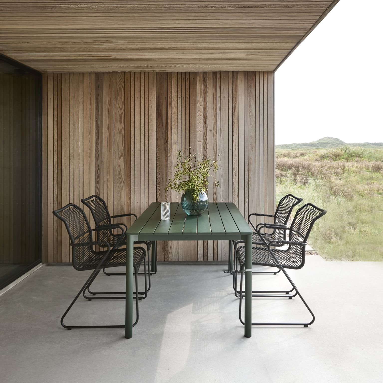 Övertäckt terrass med trädgårdsbord och trädgårdsstolar i grönt