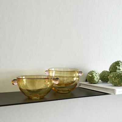 Gabriella.jpg Gula, genomskinliga skålar stående på svart hylla