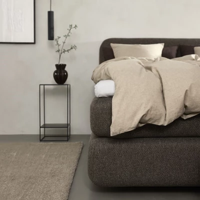 Brun seng med lys sengetøj og natbord ved siden af