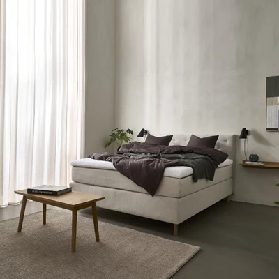 Ljusbeige dubbelsäng med brunt sänglinne i ljust sovrum