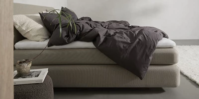 Design uden navn (16).jpg Dubbelsäng med brunt sänglinne framför vit matta i sovrum