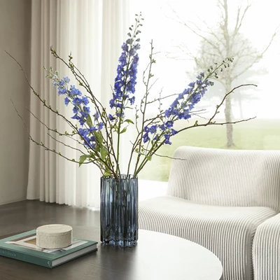 Blå vas med blåaktiga blommor stående på soffbordet