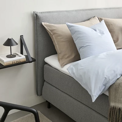 Grå Nocturne kontinentalsäng med ljust bäddset och väggmonterat sängbord