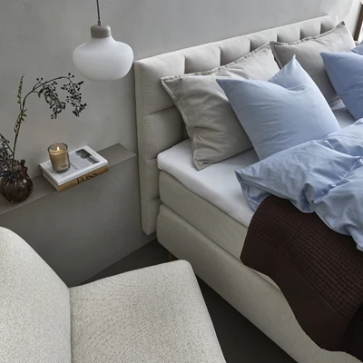 Ljus säng med blått bäddset, väggmonterat nattduksbord och taklampa