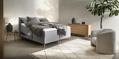 nocturne-elevationsseng. (3).jpg Grå säng i sovrum med vit matta, växt och stol