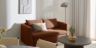 Moega.jpg Röd bäddsoffa i vardagsrum med golvlampa och tavla på väggen.