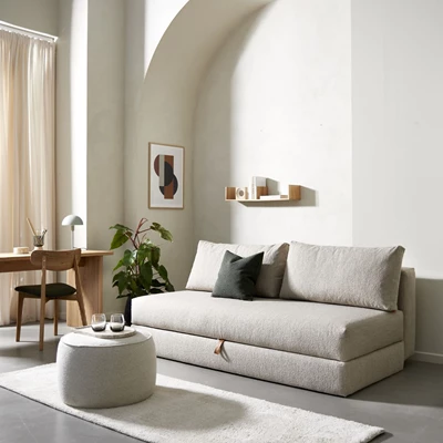 Ljus bäddsoffa i minimalistiskt vardagsrum med skrivbord och sittpuff