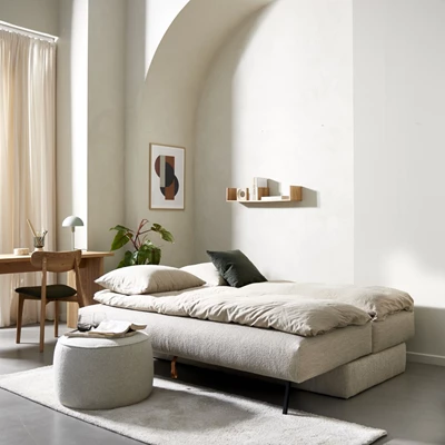 Utbäddad, ljus bäddsoffa i minimalistiskt vardagsrum med skrivbord och sittpuff