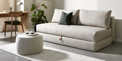 Ljus bäddsoffa i minimalistiskt vardagsrum med skrivbord och sittpuff