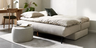 Utbäddad, ljus bäddsoffa i minimalistiskt vardagsrum med skrivbord och sittpuff