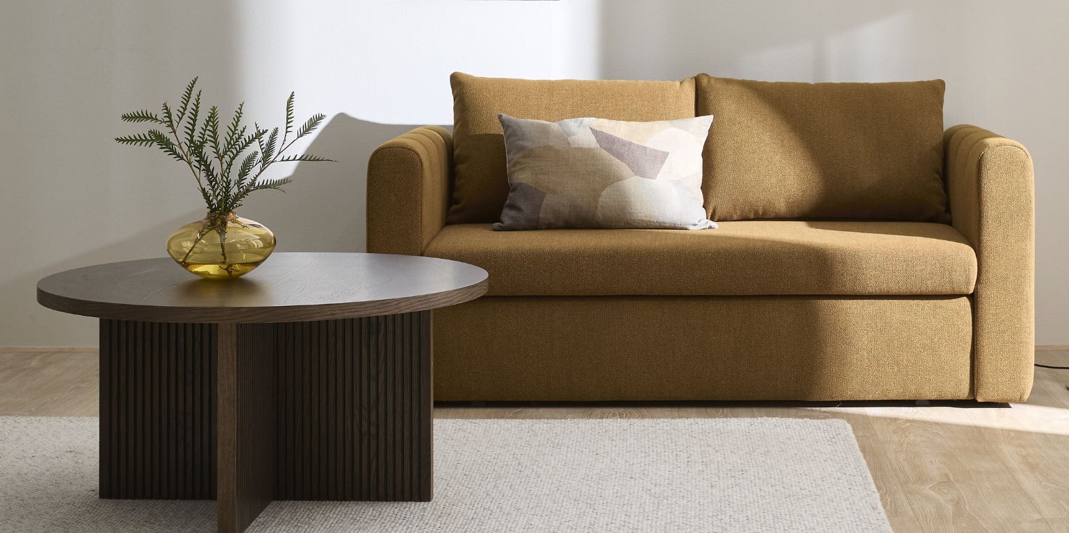 Gul bäddsoffa i vardagsrum med soffbord
