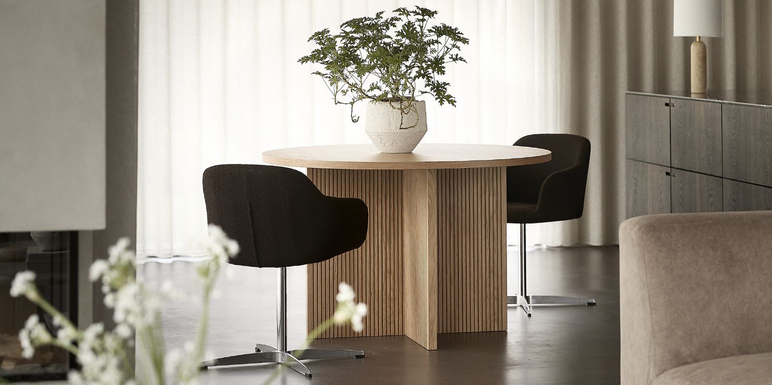 Vardagsrum med runt matbord i trä och stoppade stolar med kromunderrede.