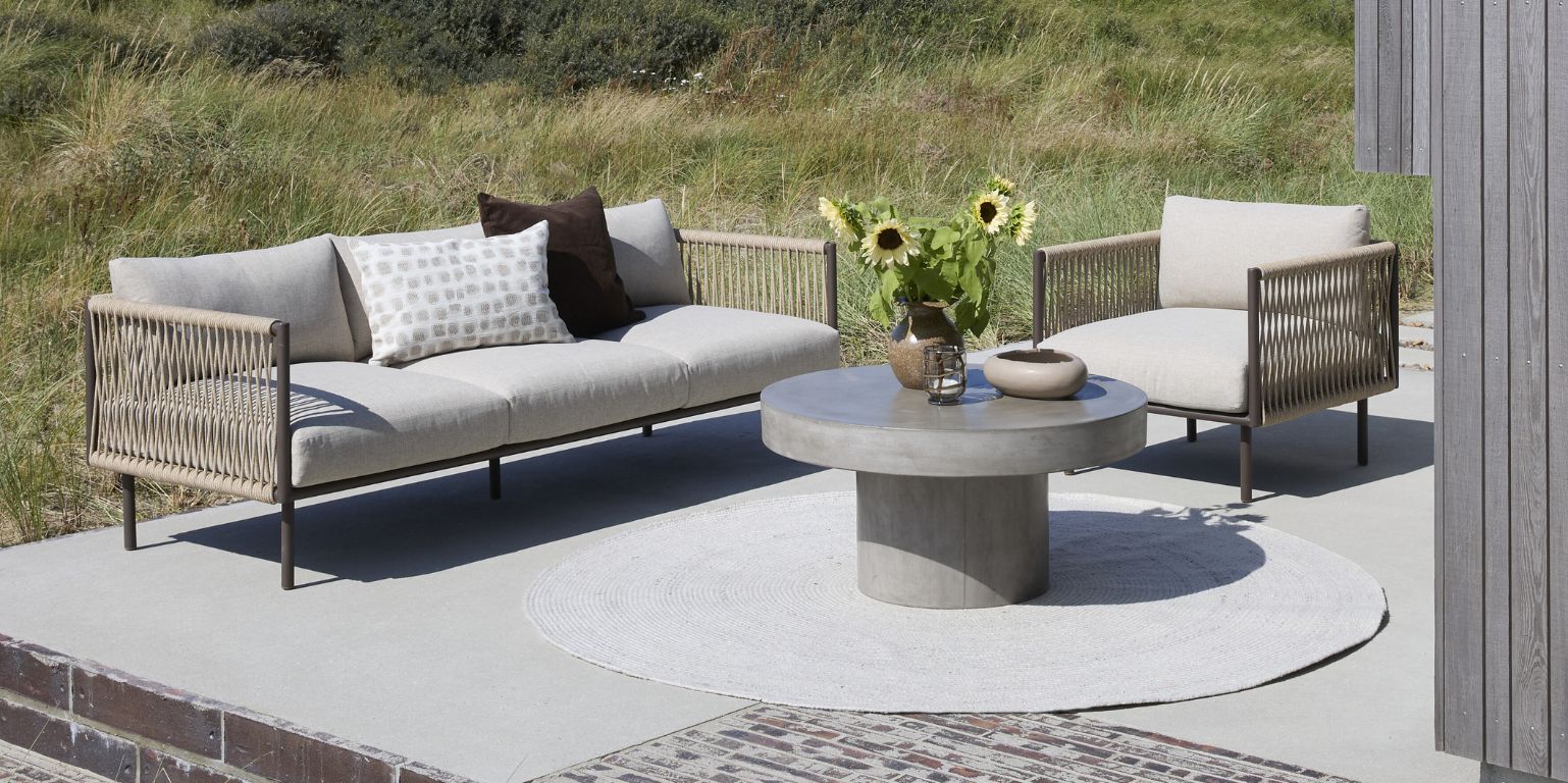 Terrassområde med loungesoffa och loungestol i gråaktiga nyanser.