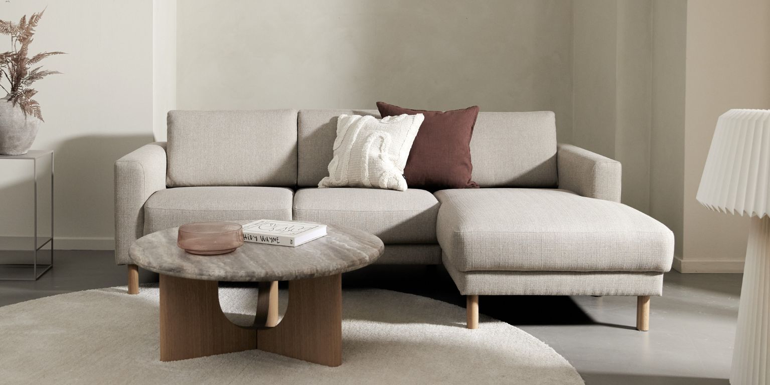 Beigefärgad soffa i ett ljust vardagsrum med soffbord, golvlampa och rund matta.