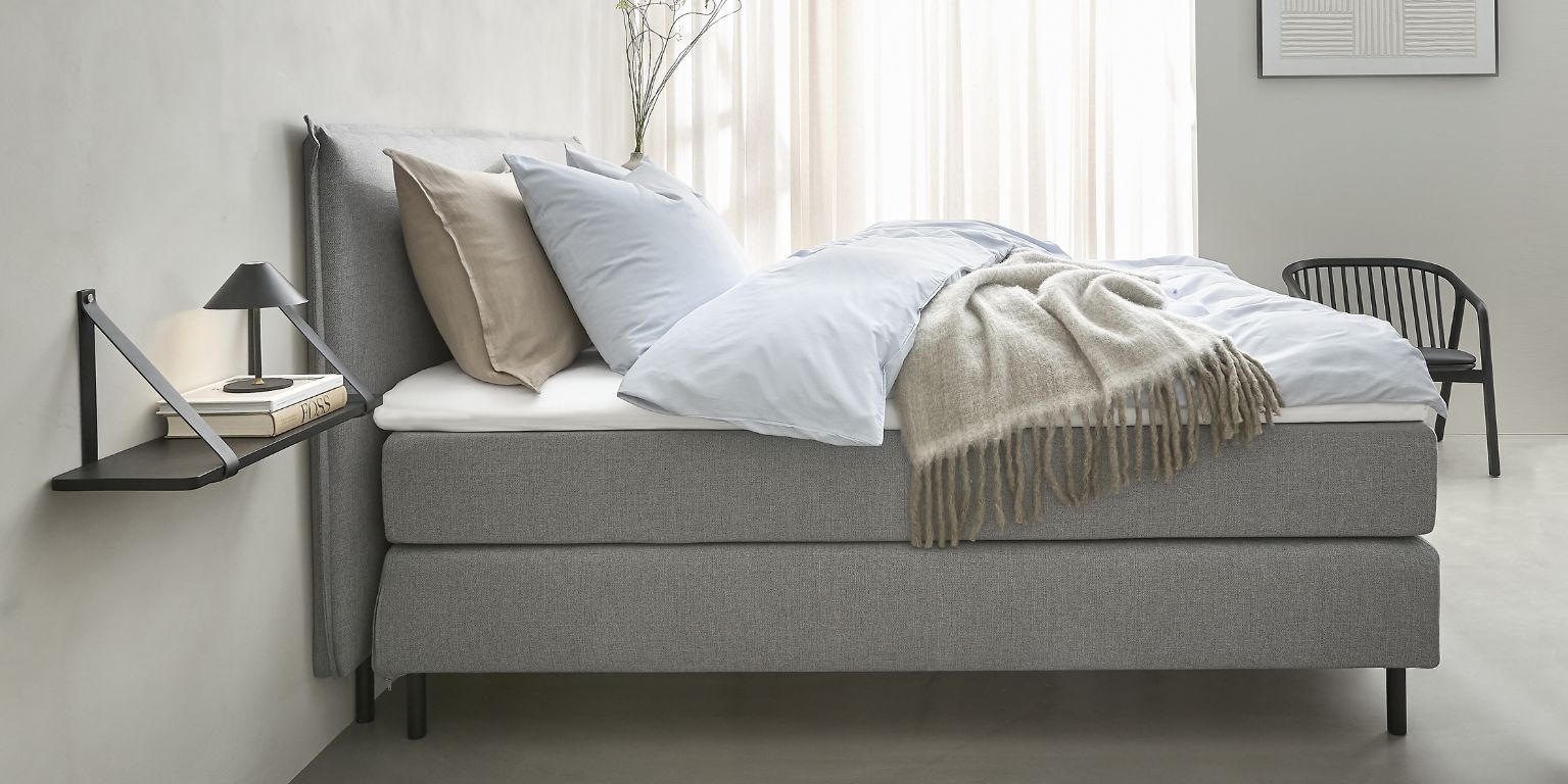 Grå kontinentalseng set fra siden i et lyst soveværelse