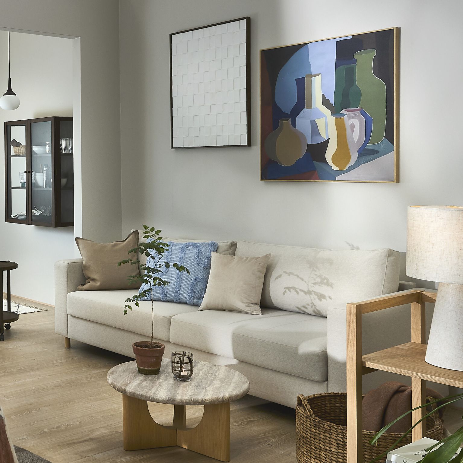 Ljus bäddsoffa i vardagsrum med soffbord, vägghängd hylla och bilder på väggen.