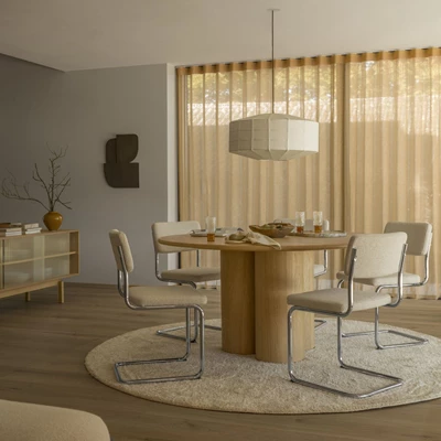 Ljust vardagsrum med runt soffbord i trä, omringat av grå stoppade stolar.