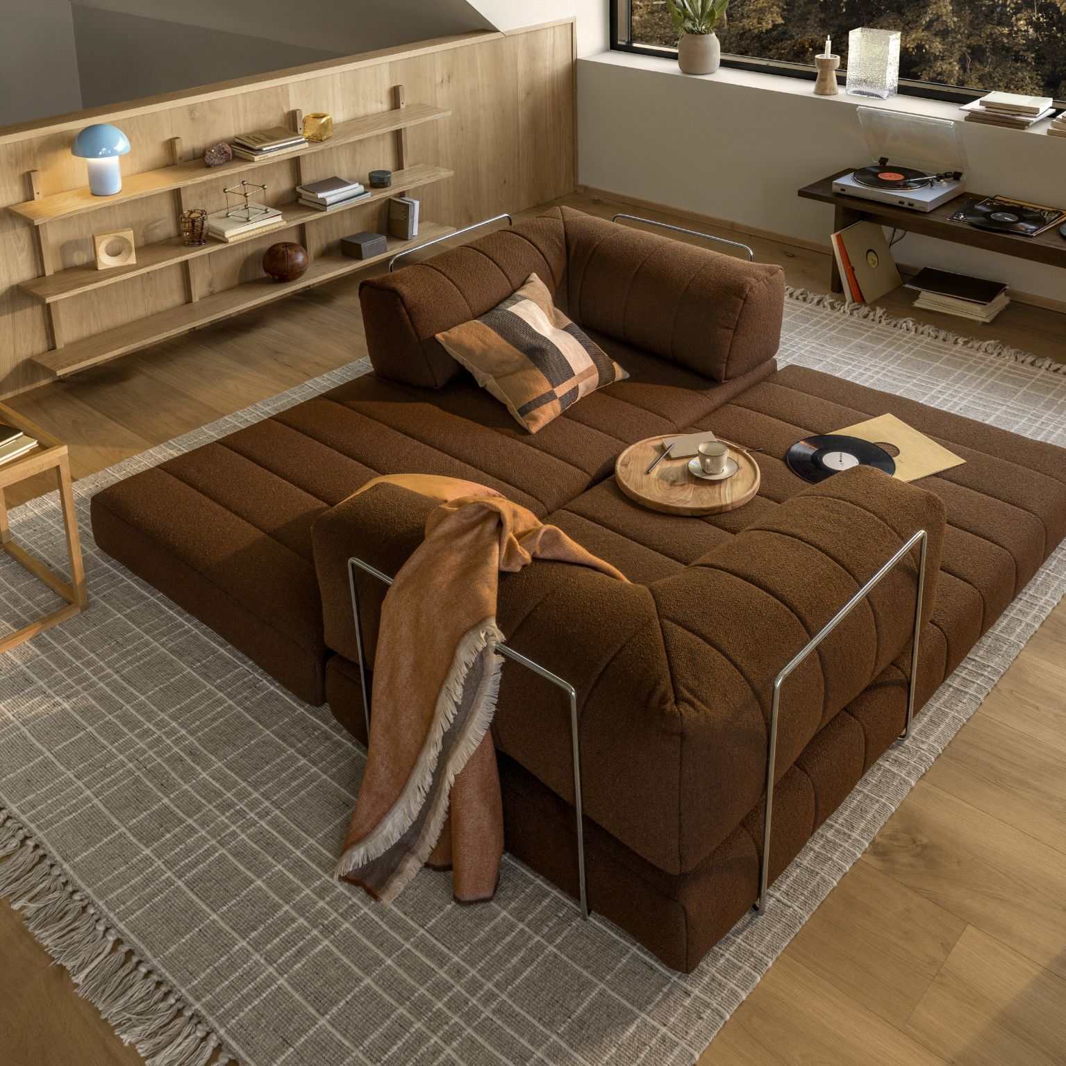 Utbäddad bäddsoffa i mörkrött placerad på matta i vardagsrum.