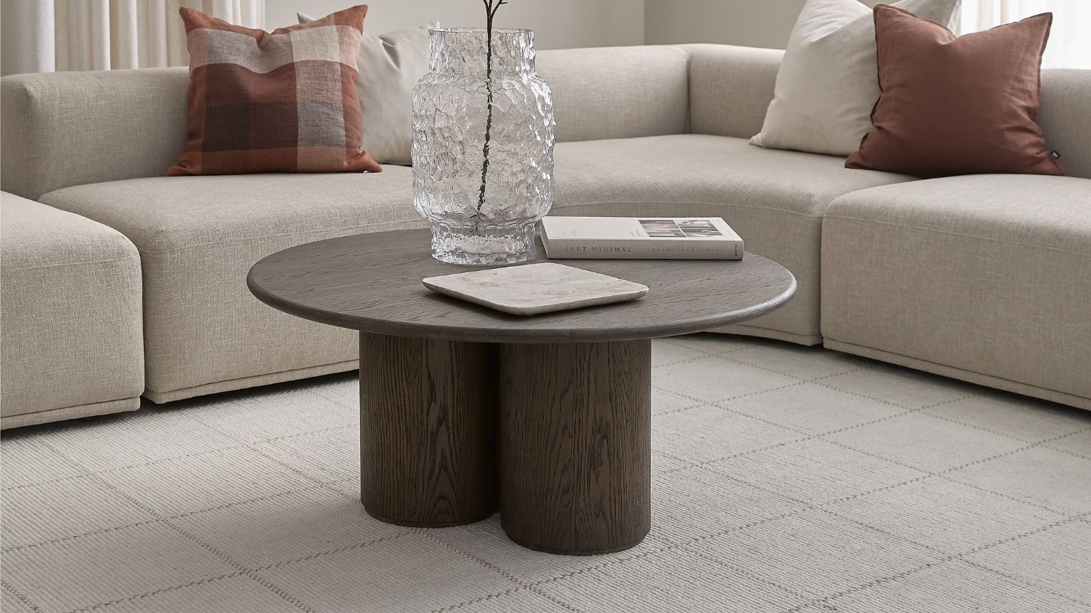 Runt soffbord med runda cylinderformade ben. Bakom bordet står en ljusgrå hörnsoffa.