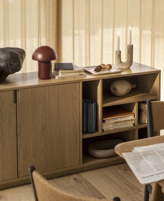 Träskänk med dörrar och öppna hyllor. Ovanpå står en röd bordslampa samt diverse prydnadsföremål.