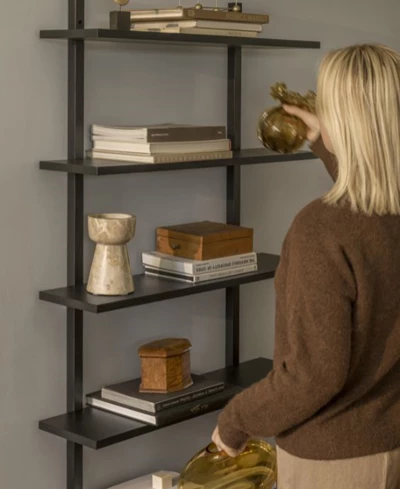 Kvinna framför svart, öppen trähylla med diverse prydnadsföremål.