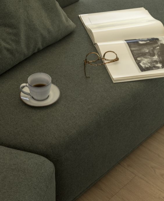 Närbild av soffa i grönt. Ovanpå står en kaffekopp, en bok och ett par glasögon.