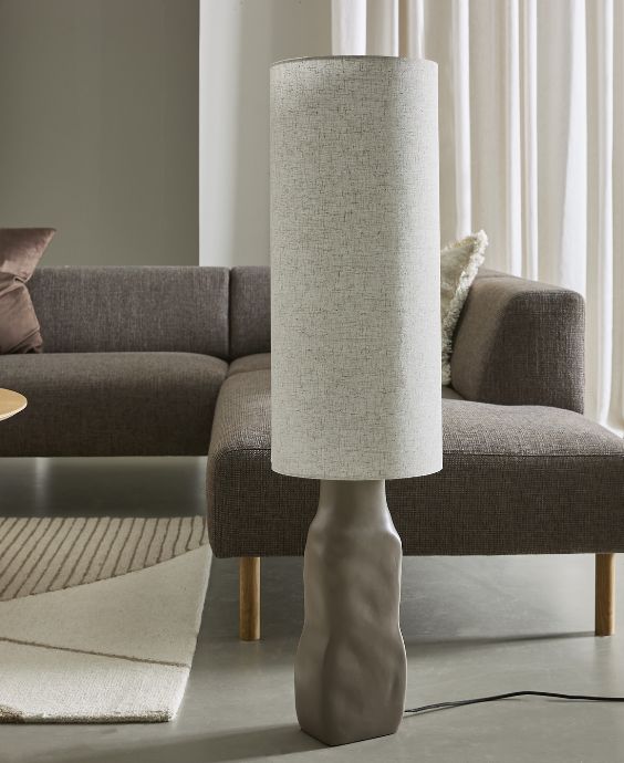 Stor golvlampa med gråaktig fot och avlång lampskärm i textil.