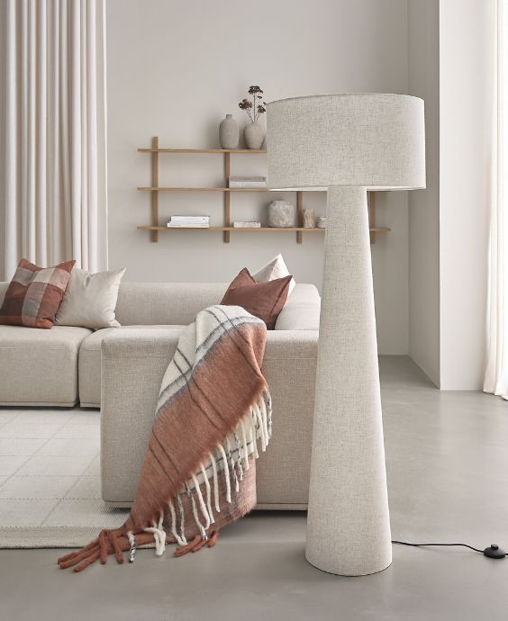 Ljus golvlampa i vitaktigt textil stående på betongolv