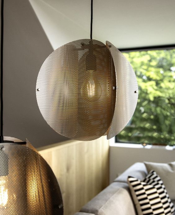 Pendel i gallerliknande material. Lampan är i metallisk färg och hänger framför fönstret.