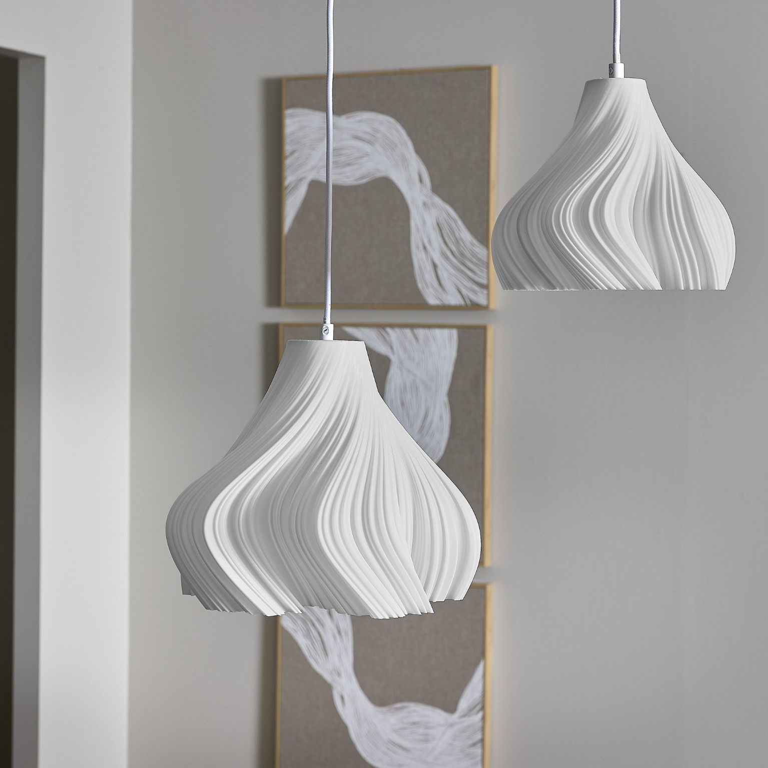 Två vita pendlar med struktur hänger framför tavelramar i grått/vitt utförande.