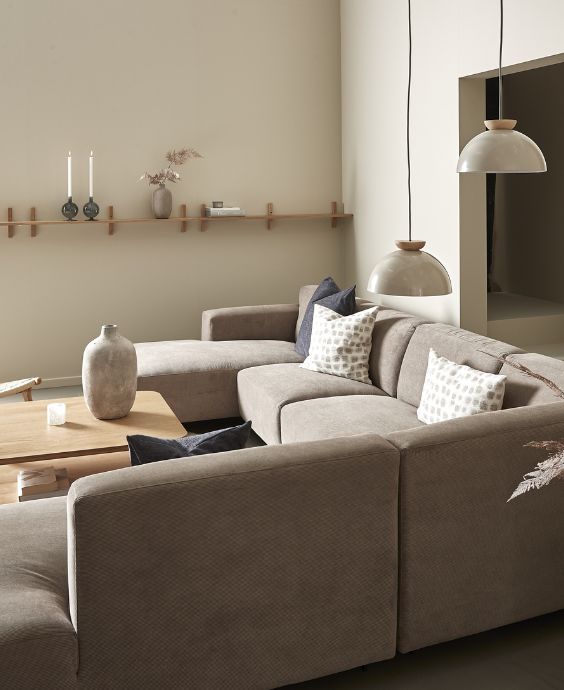 Sandfärgad hörnsoffa i vardagsrum med pendlar och hyllor på väggen