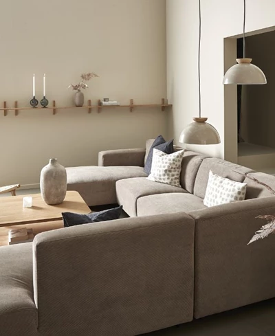 Sandfärgad hörnsoffa i vardagsrum med pendlar och hyllor på väggen