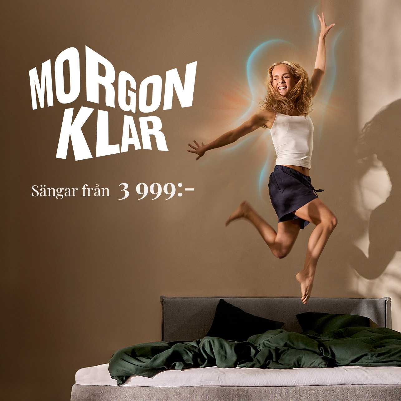 Leende kvinna hoppar upp från en bäddad säng framför texten ”Morgonklar – Sängar från 3 999:-"