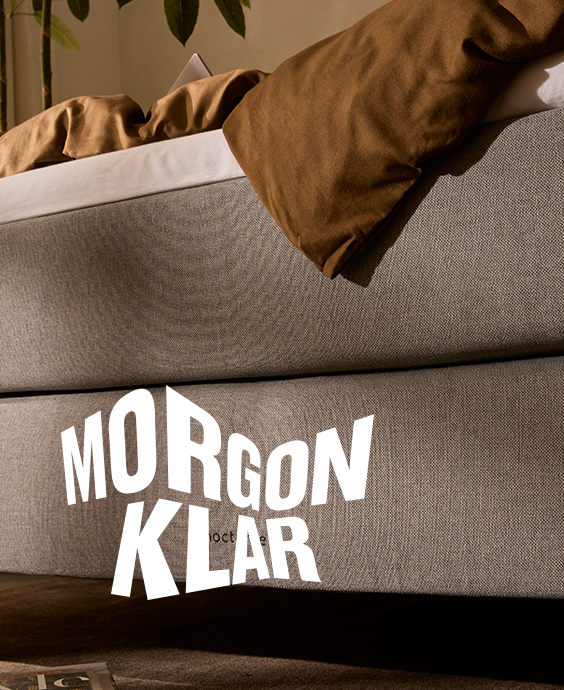 Närbild av en grå säng med en vit logotyp över, där det står Morgenklar