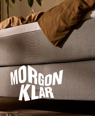 Närbild av en grå säng med en vit logotyp över, där det står Morgenklar