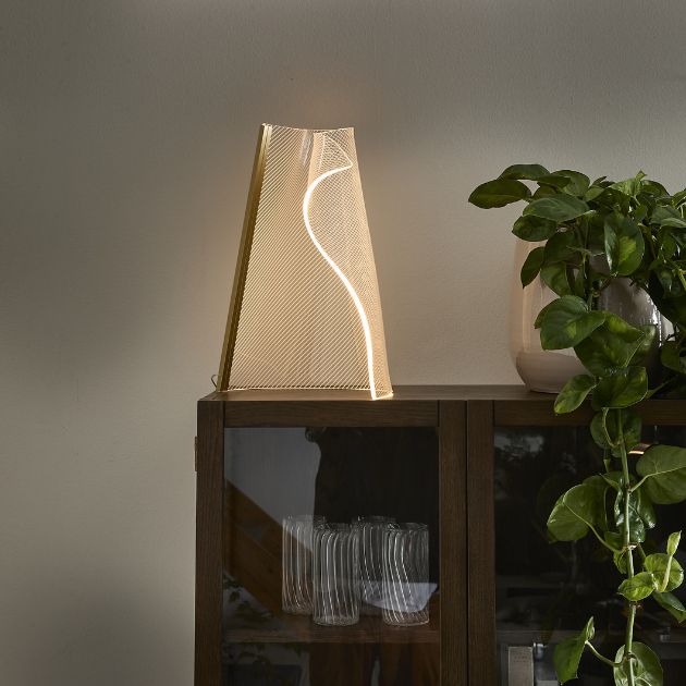 Organisk formet bordlampe i akryl stående på vitrineskab i mørkt træ