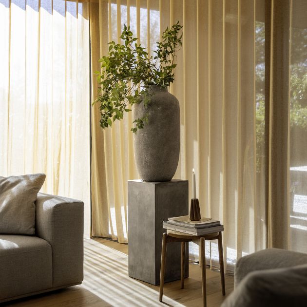 Hjørne af stue med piedestal i grå beton. Ovenpå står en stor vase med grene i