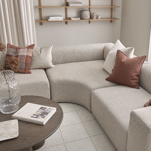 Grå modulsoffa placerad på en matta tillsammans med ett mörkbrunt soffbord och en vägghylla på väggen.