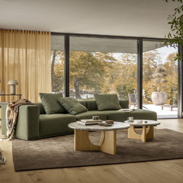 Grön modulsoffa i ett mysigt vardagsrum med två soffbord och ett stort panoramafönster bakom.