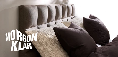 size-120x200-SE.jpg (1) Sänggavel i mörkbrunt tillsammans med kuddar i liknande nyanser.