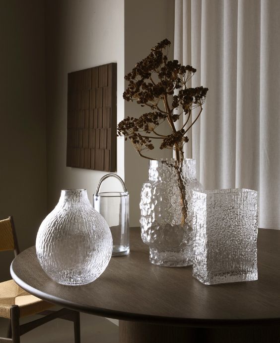 Tre genomskinliga vaser stående på ett matbord i mörkt trä.